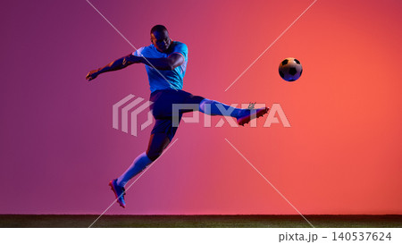 Soccer player kicking ball in blue uniform on colorful studio field. Soccer player kicking ball in blue uniform on colorful studio field. 140537624