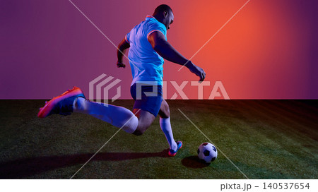 Football player taking powerful kick on grass field with colorful studio lighting. Football player taking powerful kick on grass field with colorful studio lighting. 140537654