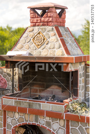 outdoor stone barbecue fireplace with brick chimney standing in a sunny backyard garden 140537703