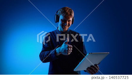 Smiling man giving thumbs up while using tablet and headphones Smiling man giving thumbs up while using tablet and headphones 140537725