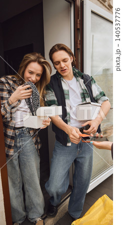 Couple unpacking online delivery boxes and paying courier at apartment entrance. 140537776