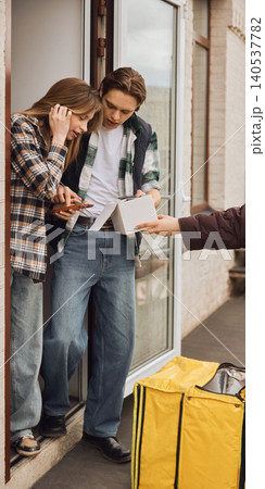 Young couple receiving home delivery package after online order at apartment door. Young couple receiving home delivery package after online order at apartment door. 140537782