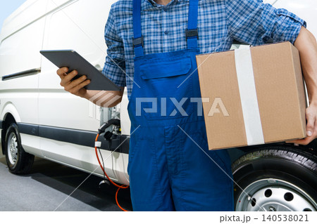 A man with a digital tablet stands next to electric delivery van. A man with a digital tablet stands next to electric delivery van. 140538021