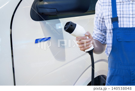 Driver with charging plug next to of electric van. Driver with charging plug next to of electric van. 140538048