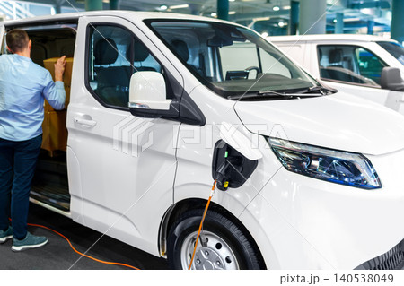 A courier removing packages from the modern electric van. The vehicle is plugged into a charging point A courier removing packages from the modern electric van. The vehicle is plugged into a charging point 140538049