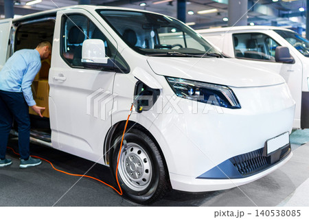 A courier removing packages from the modern electric van. The vehicle is plugged into a charging point A courier removing packages from the modern electric van. The vehicle is plugged into a charging point 140538085