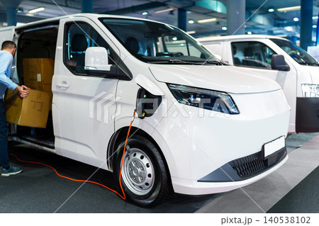 A courier removing packages from the modern electric van. The vehicle is plugged into a charging point A courier removing packages from the modern electric van. The vehicle is plugged into a charging point 140538102