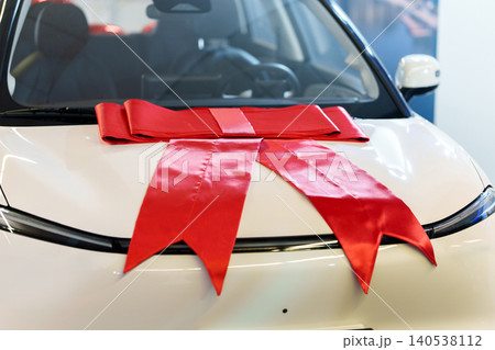Big red gift bow on the hood of a new car in showroom Big red gift bow on the hood of a new car in showroom 140538112