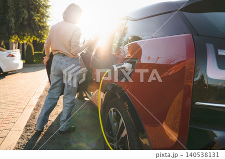 Woman with smartphone next to charging electric car Woman with smartphone next to charging electric car 140538131