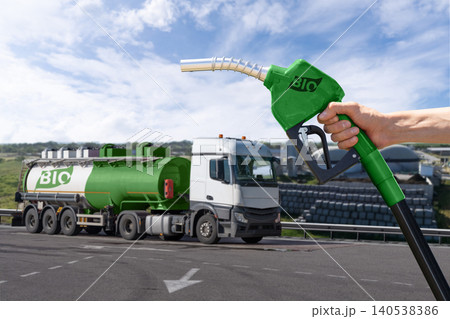 Hand with fuel nozzle with inscription BIO on a background of tank trailer with biofuel. Carbon neutral bio fuel decarbonization concept.. Hand with fuel nozzle with inscription BIO on a background of tank trailer with biofuel. Carbon neutral bio fuel decarbonization concept.. 140538386