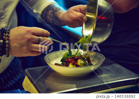 Chef pouring herb sauce over colorful vegetable salad in white ceramic bowl. Chef pouring herb sauce over colorful vegetable salad in white ceramic bowl. 140538892