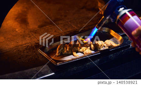 Chef searing chicken pieces with blue blowtorch flame in restaurant kitchen. Chef searing chicken pieces with blue blowtorch flame in restaurant kitchen. 140538921
