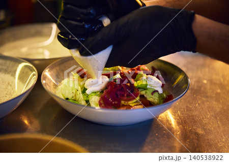 Chef piping soft cheese onto colorful salad in restaurant kitchen. 140538922