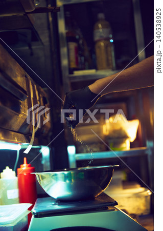 Chef sprinkling seasoning into metal mixing bowl on restaurant kitchen scale. 140538925