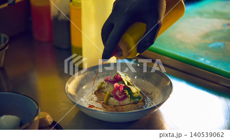 Chef adding spicy sauce to savory toast appetizer in restaurant kitchen Chef adding spicy sauce to savory toast appetizer in restaurant kitchen 140539062