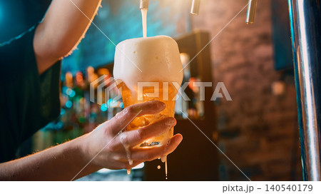 Female hand holding foamy beer glass during draft pouring. 140540179
