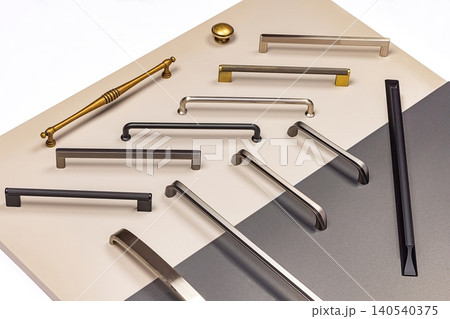 Various types of cabinet handles and pulls displayed on a neutral background in a well-lit setting Various types of cabinet handles and pulls displayed on a neutral background in a well-lit setting 140540375