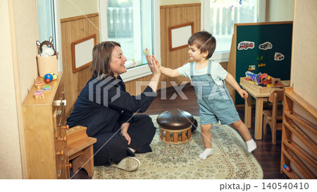 Teacher and toddler giving high five in Montessori classroom with joyful learning mood. Teacher and toddler giving high five in Montessori classroom with joyful learning mood. 140540410