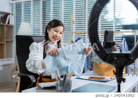 Asia vlogger woman influencer, SME retail store owner smile enjoy selling clothes live online screen smartphone and laptop work at home. Asia vlogger woman influencer, SME retail store owner smile enjoy selling clothes live online screen smartphone and laptop work at home. 140541002