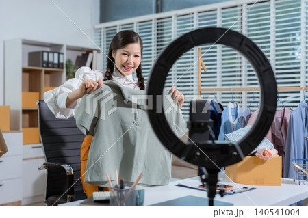 Asia vlogger woman influencer, SME retail store owner smile enjoy selling clothes live online screen smartphone and laptop work at home. 140541004