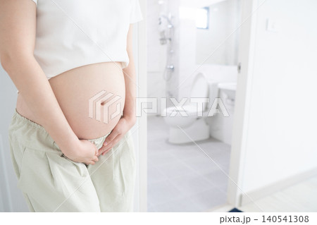 Incontinence and frequent urination during pregnancy. Pregnant woman need to pee standing by toilet in bathroom. 140541308