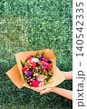 Woman Hands Holding Colorful Mixed Flower Bouquet Gift Against Green Hedge 140542335
