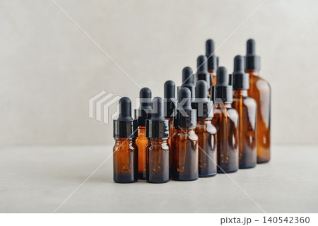 Amber glass dropper bottles of different sizes arranged in ascending order from smallest to largest on light background. Amber glass dropper bottles of different sizes arranged in ascending order from smallest to largest on light background. 140542360