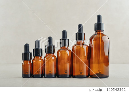 Amber glass dropper bottles of different sizes arranged in ascending order from smallest to largest on light background. Amber glass dropper bottles of different sizes arranged in ascending order from smallest to largest on light background. 140542362