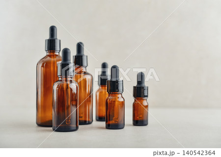 Amber glass dropper bottles of different sizes arranged in ascending order from smallest to largest on light background. Amber glass dropper bottles of different sizes arranged in ascending order from smallest to largest on light background. 140542364