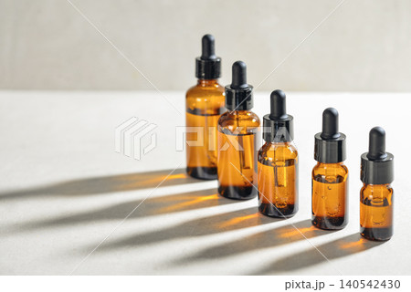 Amber glass dropper bottles of different sizes arranged in ascending order from smallest to largest on light background. 140542430