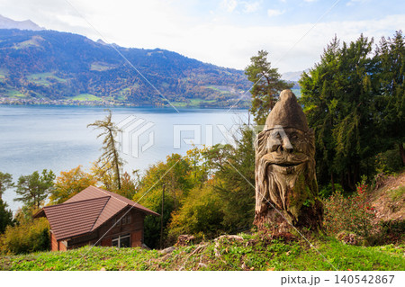 Autumn view of the Lake Thun from St. Beatus Caves entrance in Beatenberg, Bernese Oberland, Switzerland. Carved wooden statue in a foreground Autumn view of the Lake Thun from St. Beatus Caves entrance in Beatenberg, Bernese Oberland, Switzerland. Carved wooden statue in a foreground 140542867