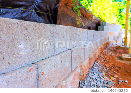 Workers are laying stones to build retaining wall in garden area surrounded by trees 140543256