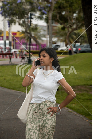 A young girl is talking on her cell phone while walking down a sidewalk A young girl is talking on her cell phone while walking down a sidewalk 140543370