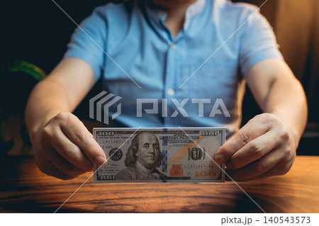 Person Holding a Hundred Dollar Bill in a Dimly Lit Room with Soft Background Lighting Person Holding a Hundred Dollar Bill in a Dimly Lit Room with Soft Background Lighting 140543573