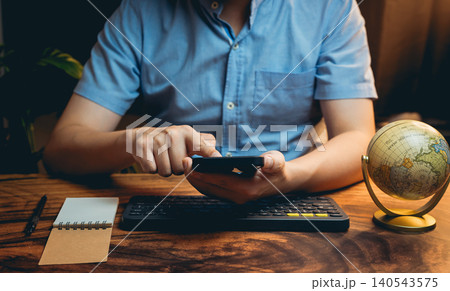 Person Using Smartphone While Sitting at Desk with Globe and Notepad in Modern Home Office Setting Person Using Smartphone While Sitting at Desk with Globe and Notepad in Modern Home Office Setting 140543575