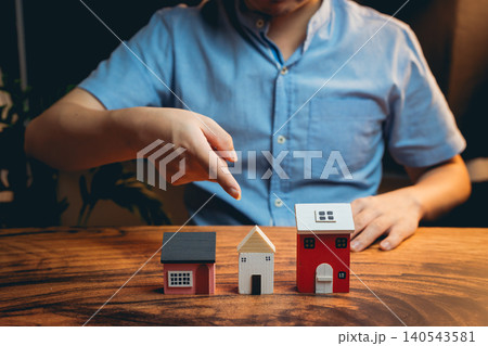 Person Demonstrating Real Estate Investment with Miniature Houses on Wooden Table Surface Person Demonstrating Real Estate Investment with Miniature Houses on Wooden Table Surface 140543581