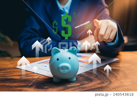 Saving money concept. Businessman in Suit Pointing to Rising Profit Graph with Piggy Bank on Table Illustrating Financial Success Concept 140543618