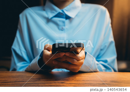 Hands Holding Smartphone with Blue Shirt in Low Light Setting Near Wooden Table Hands Holding Smartphone with Blue Shirt in Low Light Setting Near Wooden Table 140543654