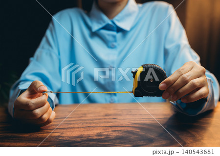 Woman Measuring Length with Tape Measure in Blue Shirt Close-Up, Focus on Hands and Measuring Tool Woman Measuring Length with Tape Measure in Blue Shirt Close-Up, Focus on Hands and Measuring Tool 140543681