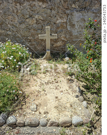 A simple stone cross is placed at a grave site surrounded by blooming wild flowers and bordered by rocks. The site is next to an old stone wall, offering a quiet spot for remembrance. A simple stone cross is placed at a grave site surrounded by blooming wild flowers and bordered by rocks. The site is next to an old stone wall, offering a quiet spot for remembrance. 140543753