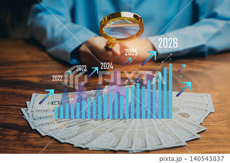 Business forecast concept. Hand holding magnifying glass over income growth chart and cash, financial analysis, revenue projection, investment insight, market trend evaluation, profit planning. 140543837