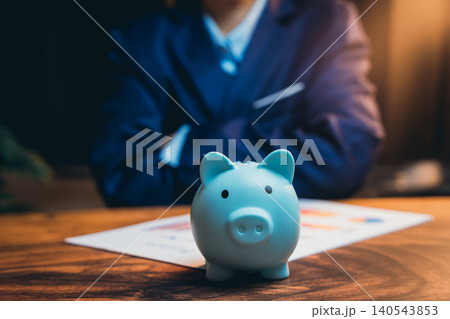 Businessman in Suit Planning Finances with Blue Piggy Bank and Financial Documents on Wooden Table Businessman in Suit Planning Finances with Blue Piggy Bank and Financial Documents on Wooden Table 140543853