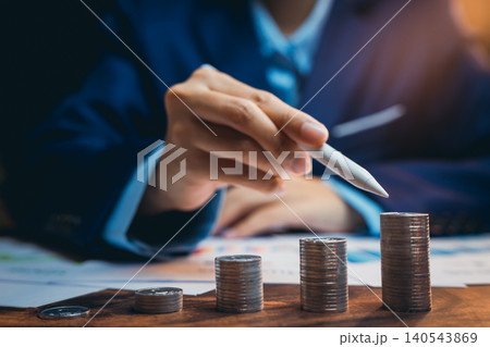 Businessman Analyzing Financial Growth with Stacks of Coins and Pen in Modern Office Setting 140543869