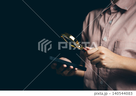 Person Holding Magnifying Glass Over Smartphone in Dark Background for Investigation or Technology Concept Person Holding Magnifying Glass Over Smartphone in Dark Background for Investigation or Technology Concept 140544083