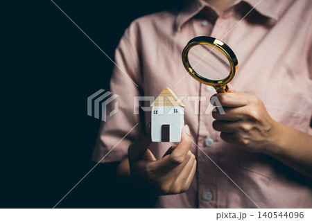 Person Holding Wooden House Model and Magnifying Glass in Dark Background for Conceptual Home Inspection and Analysis Person Holding Wooden House Model and Magnifying Glass in Dark Background for Conceptual Home Inspection and Analysis 140544096