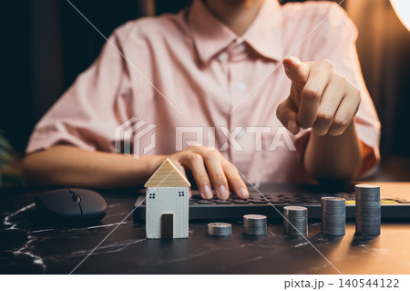 Businesswoman Analyzing Financial Data with Model House and Coins on Desk for Real Estate Investment Concept Businesswoman Analyzing Financial Data with Model House and Coins on Desk for Real Estate Investment Concept 140544122