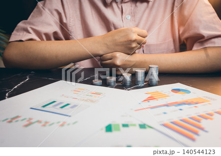 Person Analyzing Financial Data with Charts and Coins on Table in a Modern Office Environment 140544123