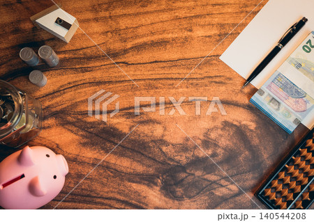 Business concept. Workspace with financial tools, piggy bank, cash notes, paper, pen, and coins arranged on wooden desk surface Business concept. Workspace with financial tools, piggy bank, cash notes, paper, pen, and coins arranged on wooden desk surface 140544208