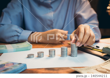 Business concept. Person Counting Stacked Coins on Table Surrounded by Banknotes and Financial Documents in Office Setting Business concept. Person Counting Stacked Coins on Table Surrounded by Banknotes and Financial Documents in Office Setting 140544211