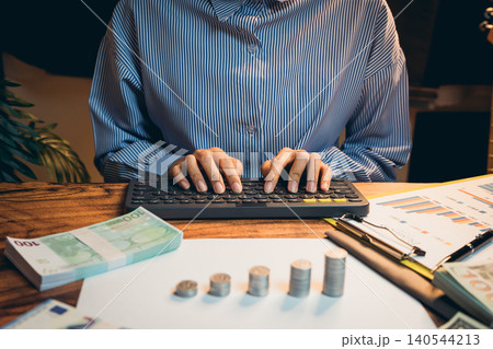 Business concept. Focused Person Working on Financial Analysis with Cash and Charts on Desk at Home Office Setting Business concept. Focused Person Working on Financial Analysis with Cash and Charts on Desk at Home Office Setting 140544213